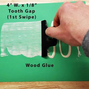 May include: A black plastic wood glue spreader with 4 inch wide teeth and 1/8 inch gaps. The spreader is being used to apply white wood glue to a green surface. The text "4" W. x 1/8" Tooth Gap (1st Swipe) Wood Glue" is visible on the surface.