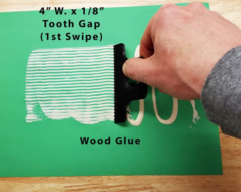 May include: A black plastic wood glue spreader with 4 inch wide teeth and 1/8 inch gaps. The spreader is being used to apply white wood glue to a green surface. The text "4" W. x 1/8" Tooth Gap (1st Swipe) Wood Glue" is visible on the surface.