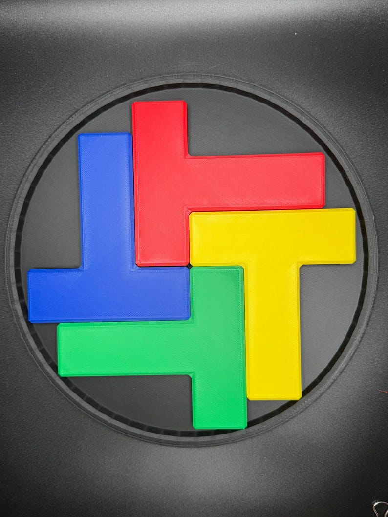 Op de afbeelding: Een ronde puzzel met vier T-vormige stukken. De stukken zijn rood, blauw, groen en geel.