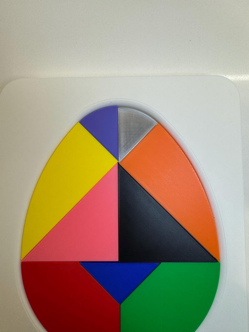 Op de afbeelding: Een kleurrijke, eivormige puzzel met acht stukken. De stukken zijn in de volgende kleuren: geel, roze, zwart, oranje, blauw, groen, paars en zilver.