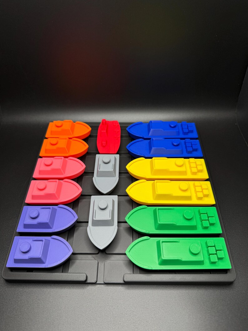 Op de afbeelding: Een set van 10 kleurrijke speelgoedbootjes, gerangschikt in een rasterpatroon op een zwart oppervlak. De bootjes zijn gemaakt van plastic en hebben verschillende kleuren, waaronder rood, oranje, geel, groen, blauw en paars. Er is ook een grijs bootje in het midden van het raster.