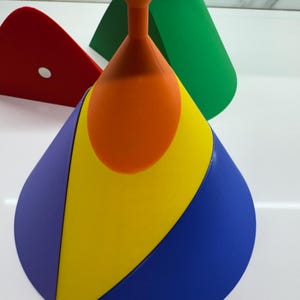 Op de afbeelding: Een veelkleurige kegel gemaakt van vier verschillende gekleurde secties: paars, geel, blauw en oranje. De kegel staat op een wit oppervlak.