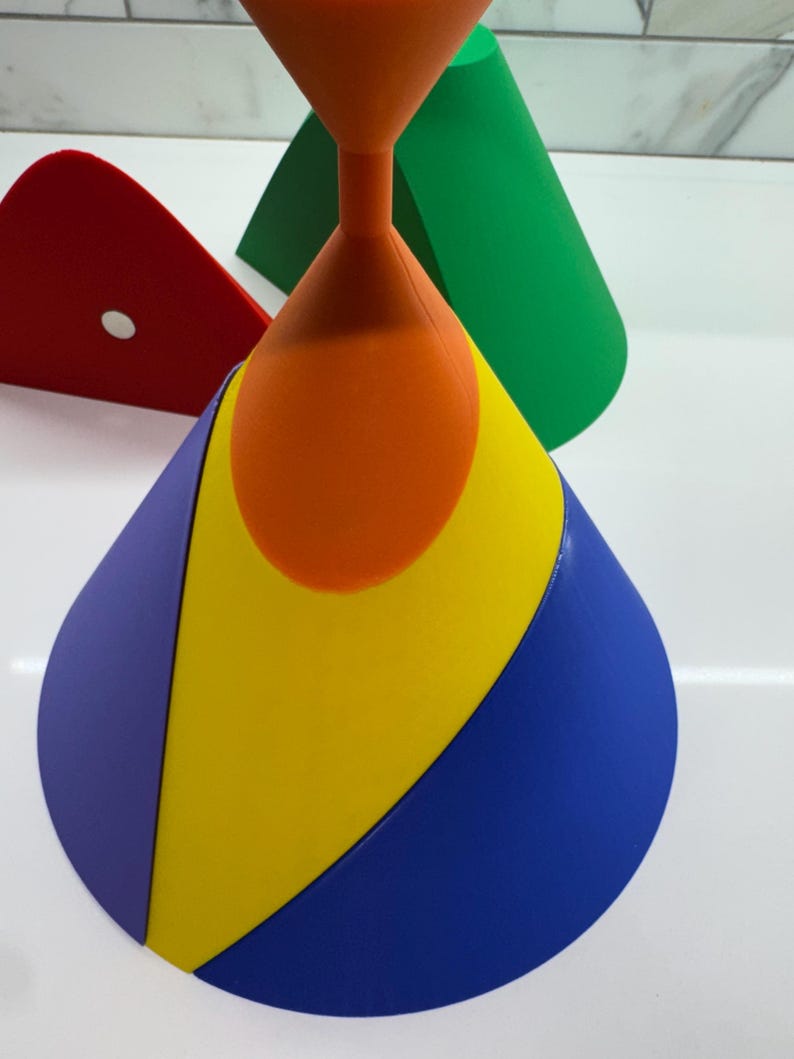 Op de afbeelding: Een veelkleurige kegel gemaakt van vier verschillende gekleurde secties: paars, geel, blauw en oranje. De kegel staat op een wit oppervlak.