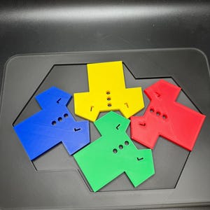 Puede incluir: Un conjunto de coloridas piezas de rompecabezas en azul, amarillo, verde y rojo. Cada pieza tiene una forma &uacute;nica con agujeros y pesta&ntilde;as, dise&ntilde;adas para encajar. Las piezas est&aacute;n dispuestas sobre una superficie gris oscuro.