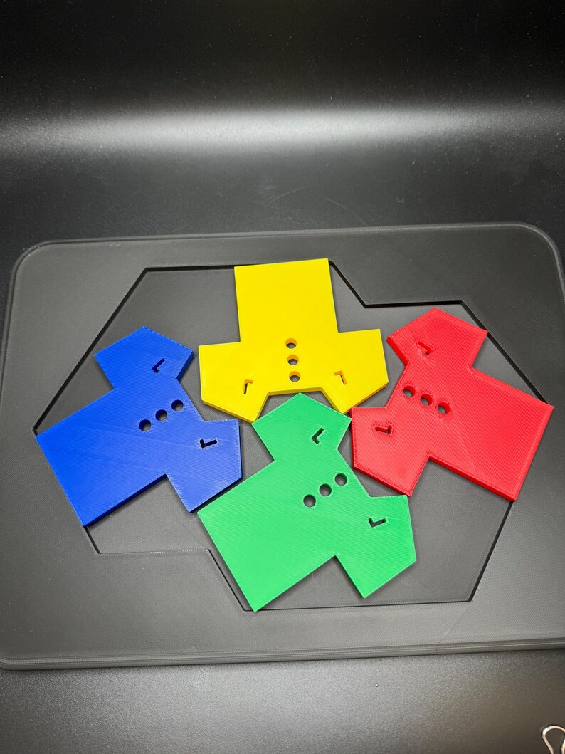 Puede incluir: Un conjunto de coloridas piezas de rompecabezas en azul, amarillo, verde y rojo. Cada pieza tiene una forma &uacute;nica con agujeros y pesta&ntilde;as, dise&ntilde;adas para encajar. Las piezas est&aacute;n dispuestas sobre una superficie gris oscuro.