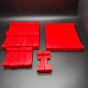 May include: Four red plastic building blocks, two are rectangular, one is square, and one is shaped like the letter 'H'.