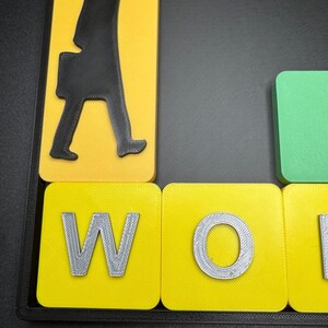 May include: Close-up of a yellow and gray word tile with the letter "W" printed on it. The tile is part of a larger set of tiles that spell out the word "WORK".
