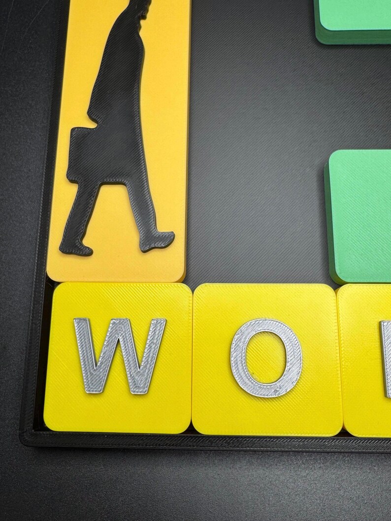May include: Close-up of a yellow and gray word tile with the letter "W" printed on it. The tile is part of a larger set of tiles that spell out the word "WORK".