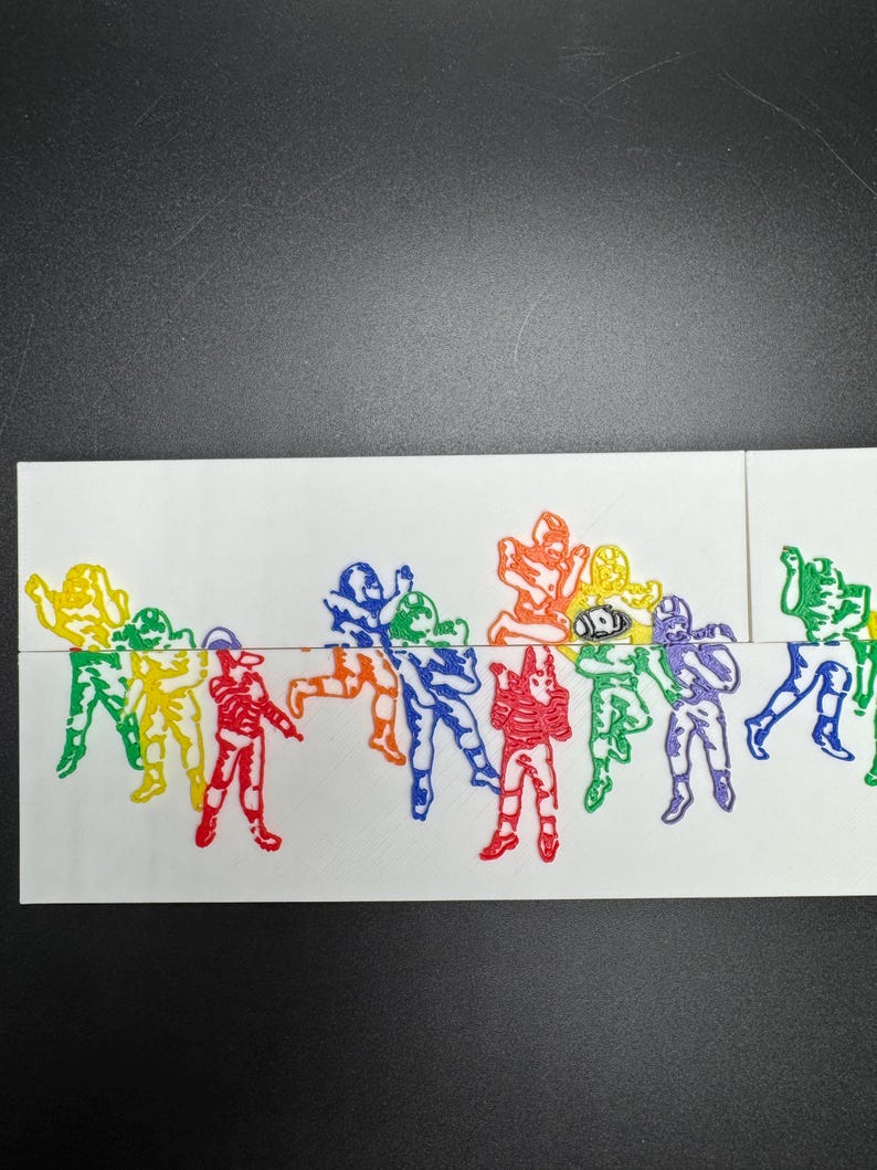 Pu&ograve; includere: Una fila di figurine di giocatori di football americano stampate in 3D di vari colori. Le figurine sono disposte in fila e sono di diversi colori, tra cui giallo, rosso, verde, blu, viola e nero.