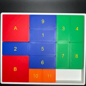 May include: A white tray with a puzzle game made of colorful tiles. The tiles are red, blue, green, and orange. The tiles have numbers and letters on them. The numbers are 1, 2, 3, 4, 5, 6, 7, 8, 9, 10, and 11. The letters are A and B.