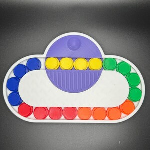 May include: A white cloud-shaped fidget toy with a purple center and a row of yellow buttons. The outer edge of the toy has a circle of blue, red, and green buttons.
