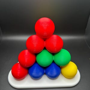 May include: A pyramid-shaped puzzle made of colorful spheres. The puzzle is made of red, green, blue, and yellow spheres. The puzzle is on a white base.
