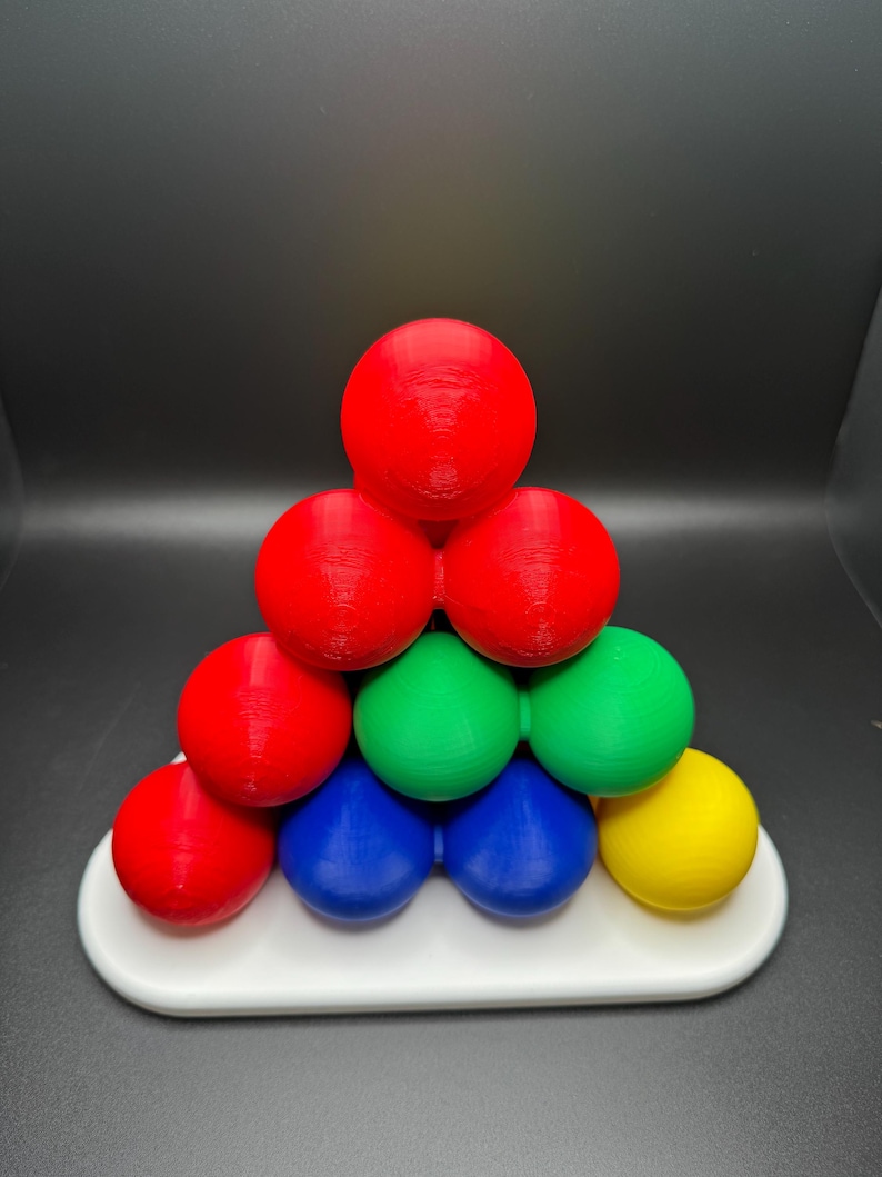 May include: A pyramid-shaped puzzle made of colorful spheres. The puzzle is made of red, green, blue, and yellow spheres. The puzzle is on a white base.
