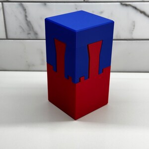 May include: A two-piece puzzle box with a blue top and a red bottom. The top has two cutouts that fit into the bottom.