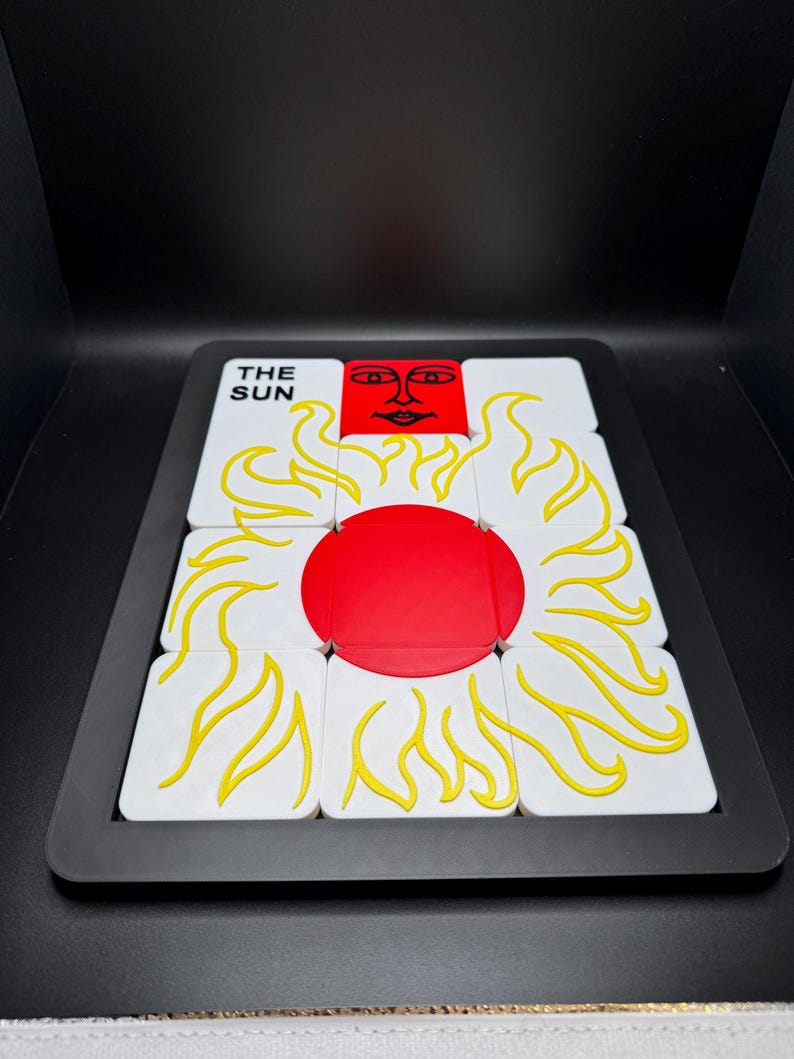 May include: A puzzle featuring a sun design. The puzzle has a black frame and is composed of white tiles with yellow flames and a red sun in the center. The text "THE SUN" is visible on one of the tiles.
