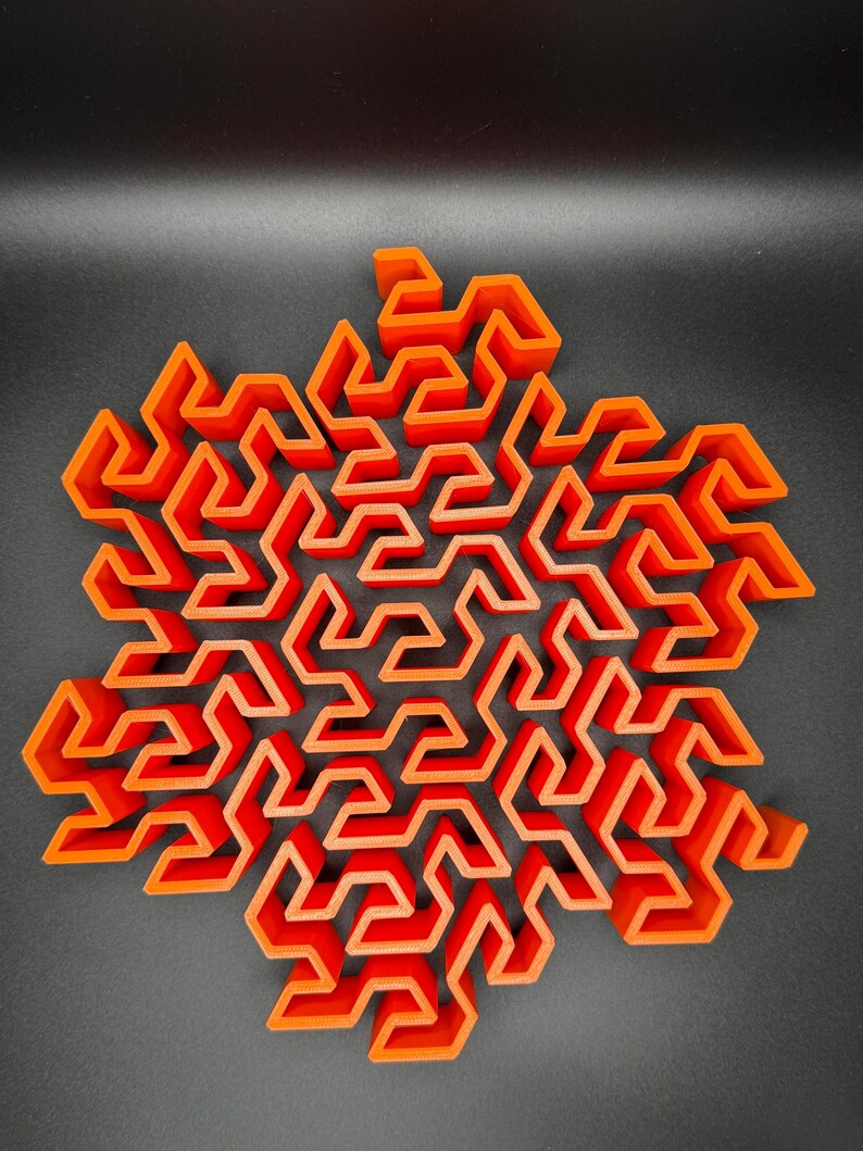 May include: A 3D printed orange geometric maze in the shape of a snowflake.