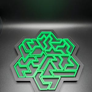 May include: A green 3D printed snowflake design with a black background. The snowflake is made up of a series of interlocking shapes.