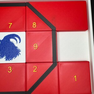 May include: A red puzzle with black trim and yellow numbers 1 through 9. The puzzle is arranged in a grid pattern with a goat illustration in the center.