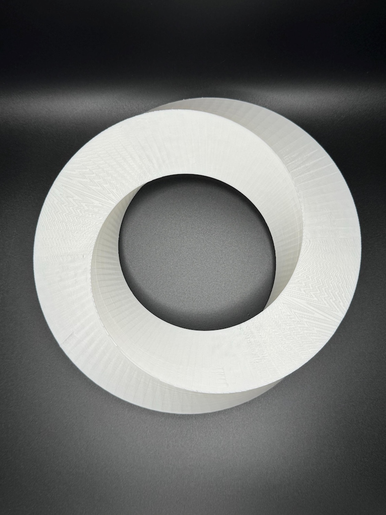 May include: White, three-dimensional, abstract sculpture in the shape of a Mobius strip. The sculpture is made of a smooth, white material and has a circular shape.