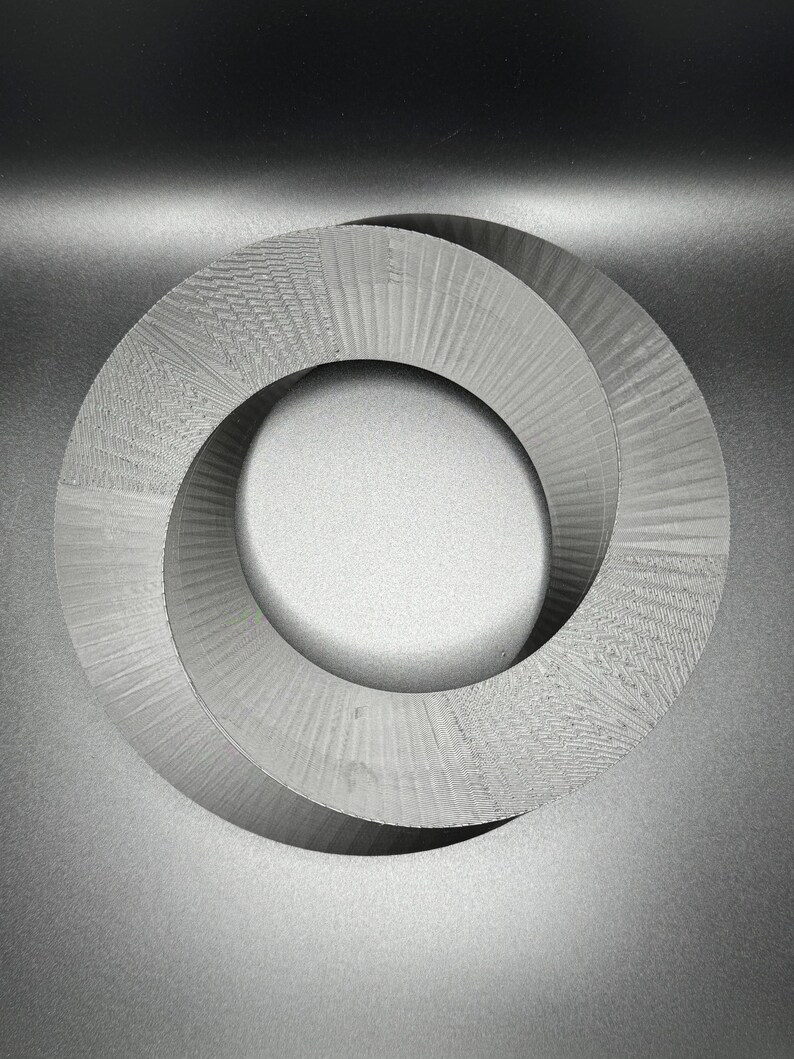May include: A gray, 3D printed, Mobius strip sculpture. The sculpture is made of two interlocking rings that form a continuous loop.