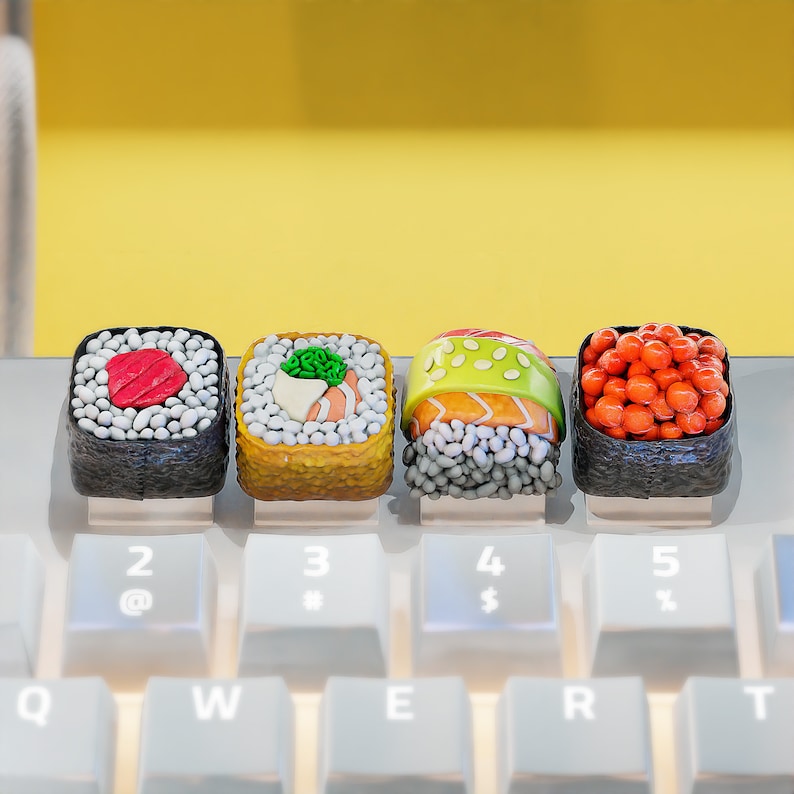 May include: Four colorful sushi rolls made of play dough. The rolls are arranged in a row on a white keyboard. The rolls are decorated with red, green, and yellow accents.