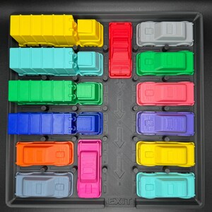 May include: A toy parking lot featuring a variety of brightly coloured vehicles. The set includes a yellow lorry, a teal truck, a green truck, a blue truck, an orange car, a grey car, a red truck, a pink car, a grey car, a green car, a pink car, a yellow car, and a teal car. The word "EXIT" is visible.