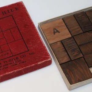 K&ouml;nnte beinhalten: Eine rote Schachtel mit den Worten "Slide A While" und "Rochester Puzzle Co." darauf. Die Schachtel enth&auml;lt ein Holzpuzzle mit dem Wort "Door" auf einem der Teile.