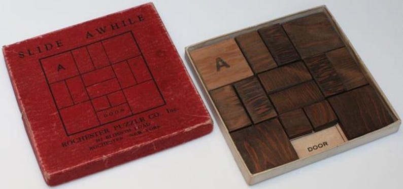 K&ouml;nnte beinhalten: Eine rote Schachtel mit den Worten "Slide A While" und "Rochester Puzzle Co." darauf. Die Schachtel enth&auml;lt ein Holzpuzzle mit dem Wort "Door" auf einem der Teile.