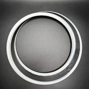 May include: A circular object with a white outer ring, a black inner ring, and a textured black section. The object is set against a black background, creating a contrast that highlights its design.