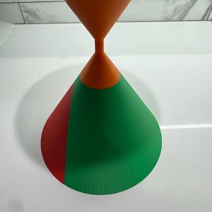 Op de afbeelding: Een veelkleurig, kegelvormig object met een geel, oranje, rood en groen ontwerp. De kegel is gemaakt van een glad, hard materiaal en heeft een glanzende afwerking.