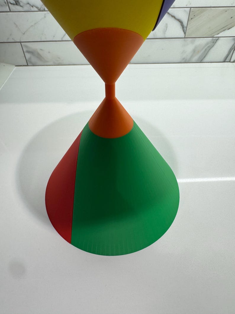 Op de afbeelding: Een veelkleurig, kegelvormig object met een geel, oranje, rood en groen ontwerp. De kegel is gemaakt van een glad, hard materiaal en heeft een glanzende afwerking.