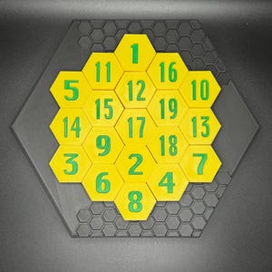 Puede incluir: Un rompecabezas hexagonal amarillo con n&uacute;meros verdes del 1 al 19 en cada pieza. El rompecabezas est&aacute; sobre una base hexagonal negra.