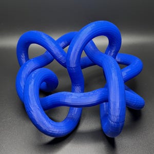 K&ouml;nnte beinhalten: Eine blaue 3D-gedruckte Knotenskulptur. Der Knoten besteht aus einem einzigen durchgehenden St&uuml;ck Plastik und ist in einem komplexen Muster verdreht und gewendet.