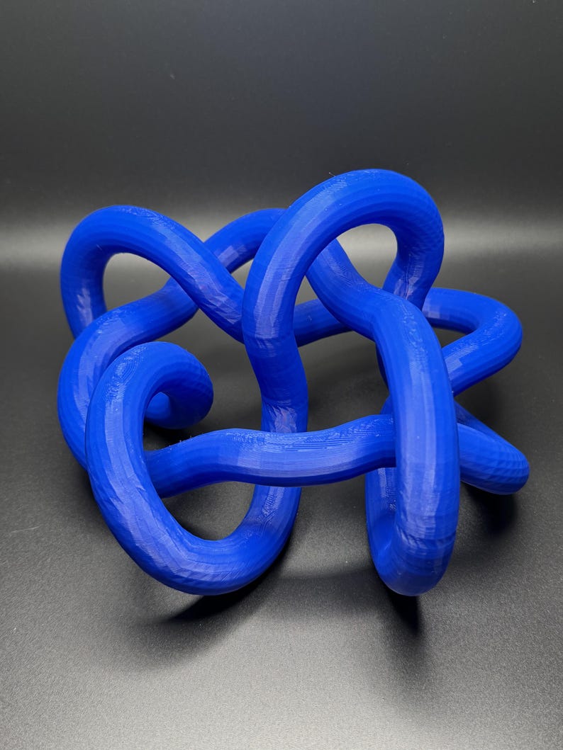 K&ouml;nnte beinhalten: Eine blaue 3D-gedruckte Knotenskulptur. Der Knoten besteht aus einem einzigen durchgehenden St&uuml;ck Plastik und ist in einem komplexen Muster verdreht und gewendet.