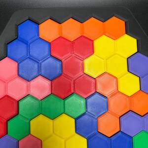 May include: A colorful hexagonal puzzle with pieces in shades of red, orange, yellow, green, blue, and pink. The puzzle is made of plastic and has a textured surface.