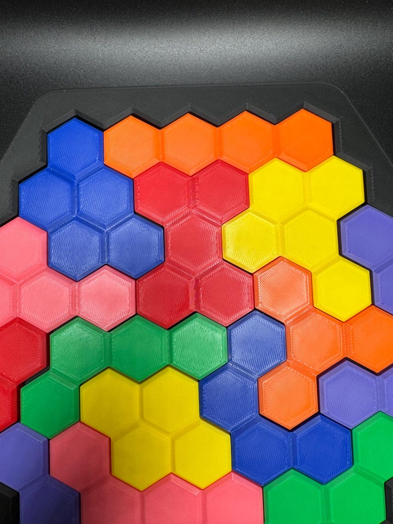 May include: A colorful hexagonal puzzle with pieces in shades of red, orange, yellow, green, blue, and pink. The puzzle is made of plastic and has a textured surface.