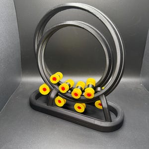 May include: A black, 3D-printed abacus-style toy with a double-loop track. The toy features yellow and red beads that move along the track. The base is also black, and the background is a dark gray.