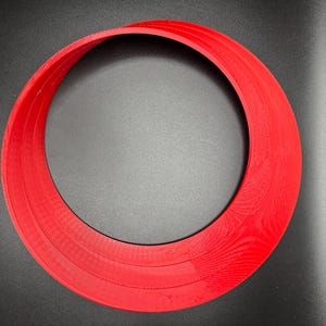May include: A red plastic ring with three layers, creating a circular shape with a hole in the centre.