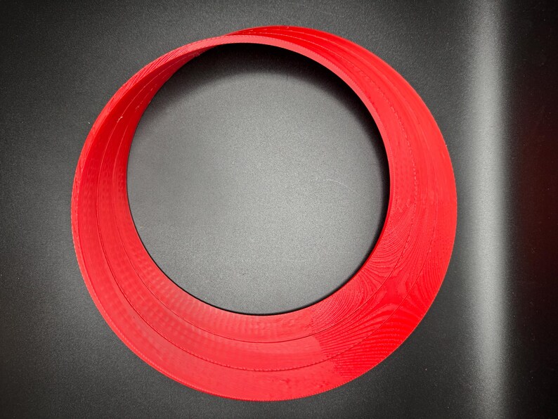 May include: A red plastic ring with three layers, creating a circular shape with a hole in the centre.
