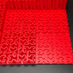 May include: A red plastic puzzle mat with interlocking pieces in the shape of a plus sign. The mat is made up of multiple sections that can be connected together.