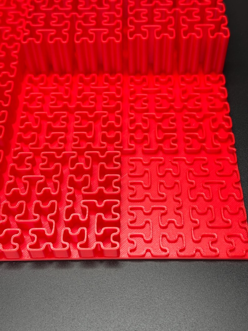 May include: A red plastic puzzle mat with interlocking pieces in the shape of a plus sign. The mat is made up of multiple sections that can be connected together.