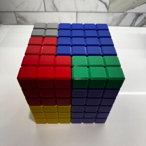 May include: A cube made of colorful blocks. The top layer is gray, blue, green, and blue. The second layer is red, blue, and blue. The bottom layer is yellow, blue, and blue.