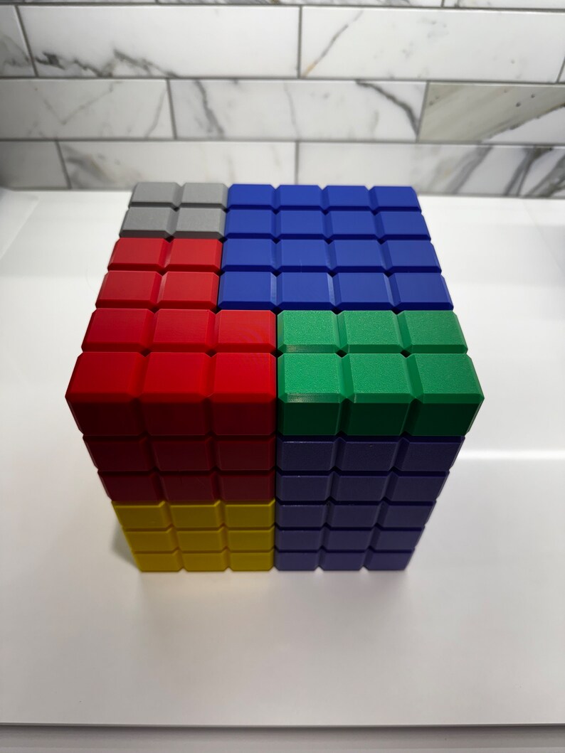 May include: A cube made of colorful blocks. The top layer is gray, blue, green, and blue. The second layer is red, blue, and blue. The bottom layer is yellow, blue, and blue.