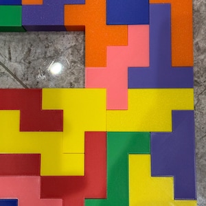 May include: A colourful puzzle made of various geometric shapes in red, yellow, green, blue, orange, and purple. The puzzle pieces are arranged in a pattern to create a square shape.