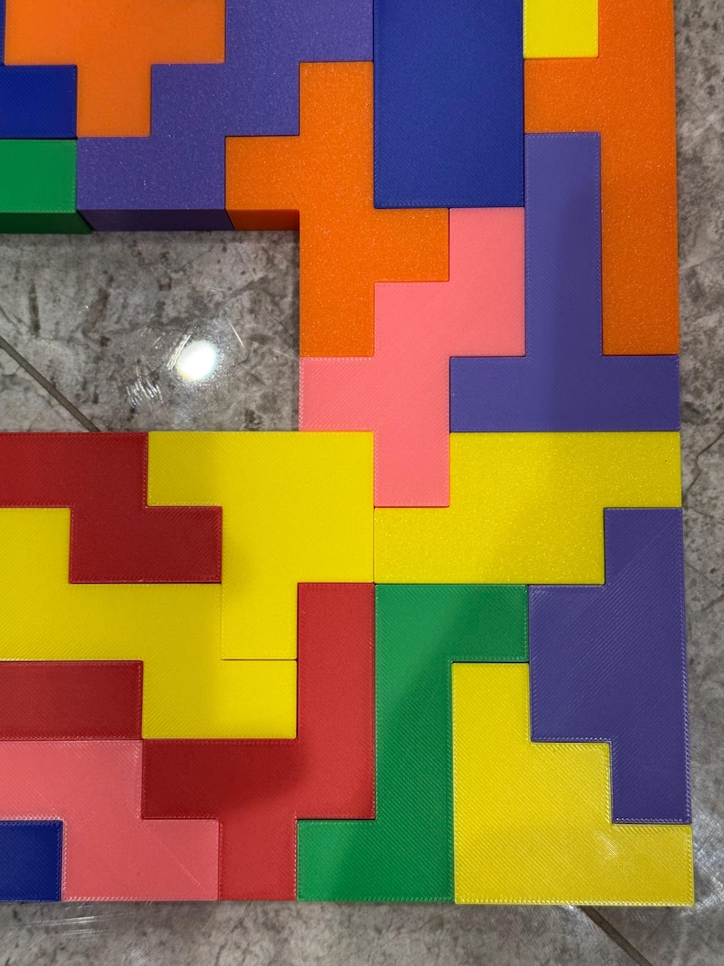 May include: A colourful puzzle made of various geometric shapes in red, yellow, green, blue, orange, and purple. The puzzle pieces are arranged in a pattern to create a square shape.