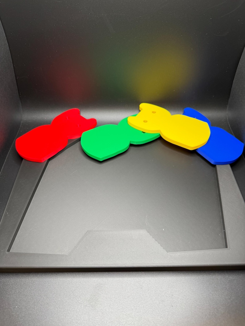 May include: Four colorful, abstract cat-shaped acrylic coasters in red, green, yellow, and blue. The coasters are arranged in a row, with each one slightly overlapping the next. The background is black.