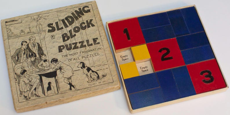 May include: A wooden game box with a sliding block puzzle. The box is brown with a white label that reads "Sliding Block Puzzle, The Most Fascinating of All Puzzles". The puzzle board is made of wood and has blue, red, and yellow squares with numbers 1, 2, and 3.