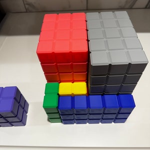 May include: A set of colorful building blocks in red, gray, yellow, green, and blue. The blocks are stacked on top of each other to form a tower.