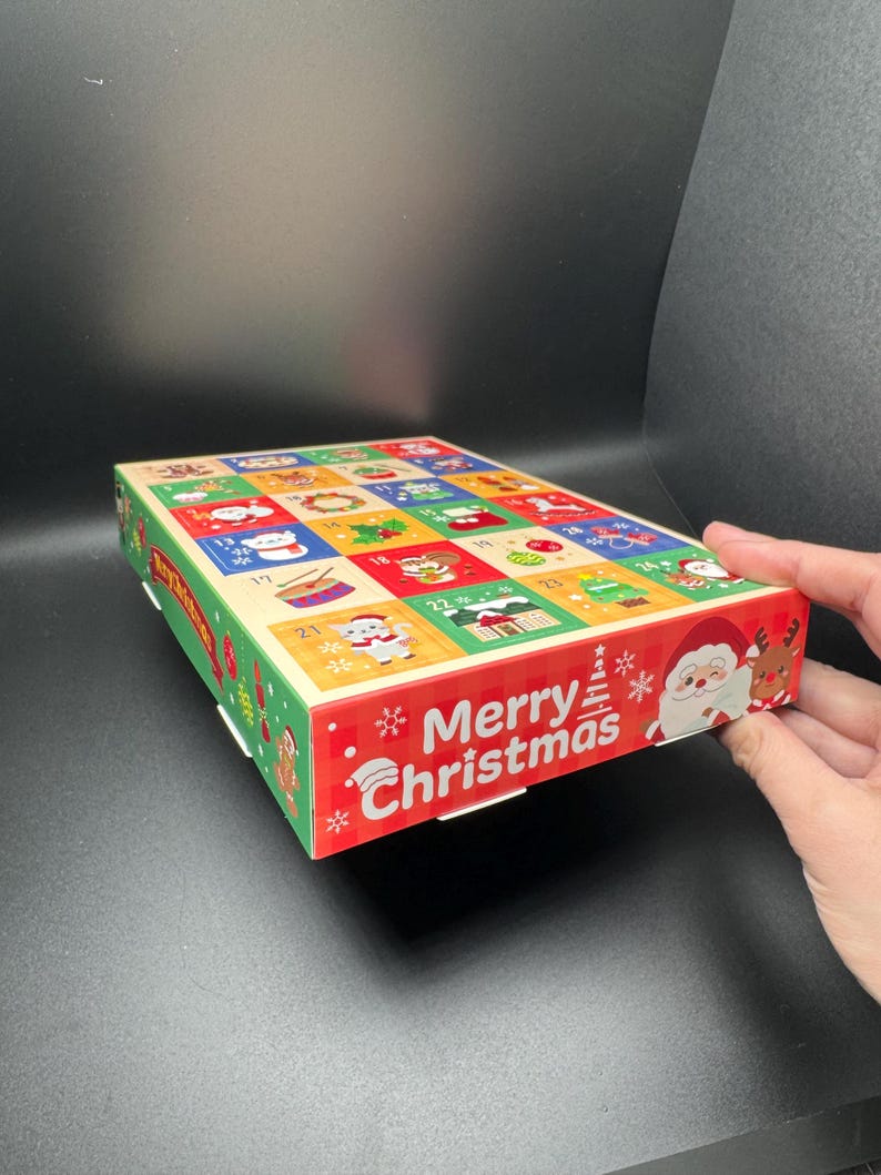 May include: A colorful Christmas advent calendar with numbered doors. The box features a red border with "Merry Christmas" text and festive illustrations of Santa Claus, reindeer, and snowflakes. The top has 24 decorated squares.