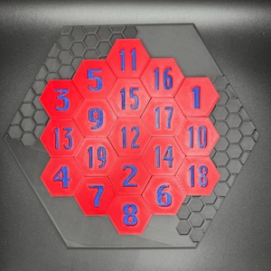Puede incluir: Un rompecabezas hexagonal rojo con n&uacute;meros azules del 1 al 19. El rompecabezas est&aacute; sobre un fondo hexagonal negro.